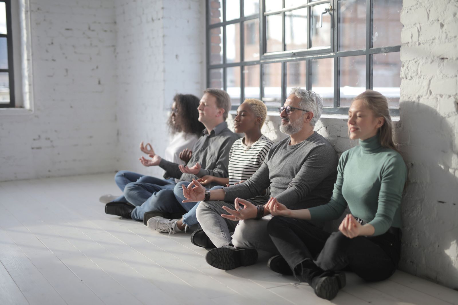 A diverse group of coworkers meditating together during a break in a bright modern office.